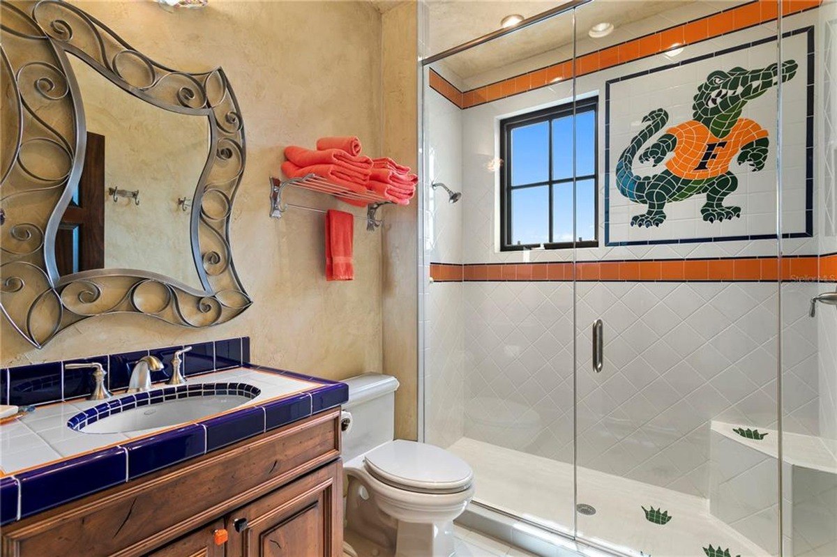 Bathroom features a glass-enclosed shower with a tiled alligator mascot, a vanity with a blue tile backsplash, and an ornate mirror.