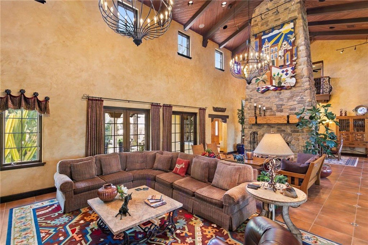 Large living area features a sectional sofa, a stone fireplace, and high ceilings with exposed wooden beams.