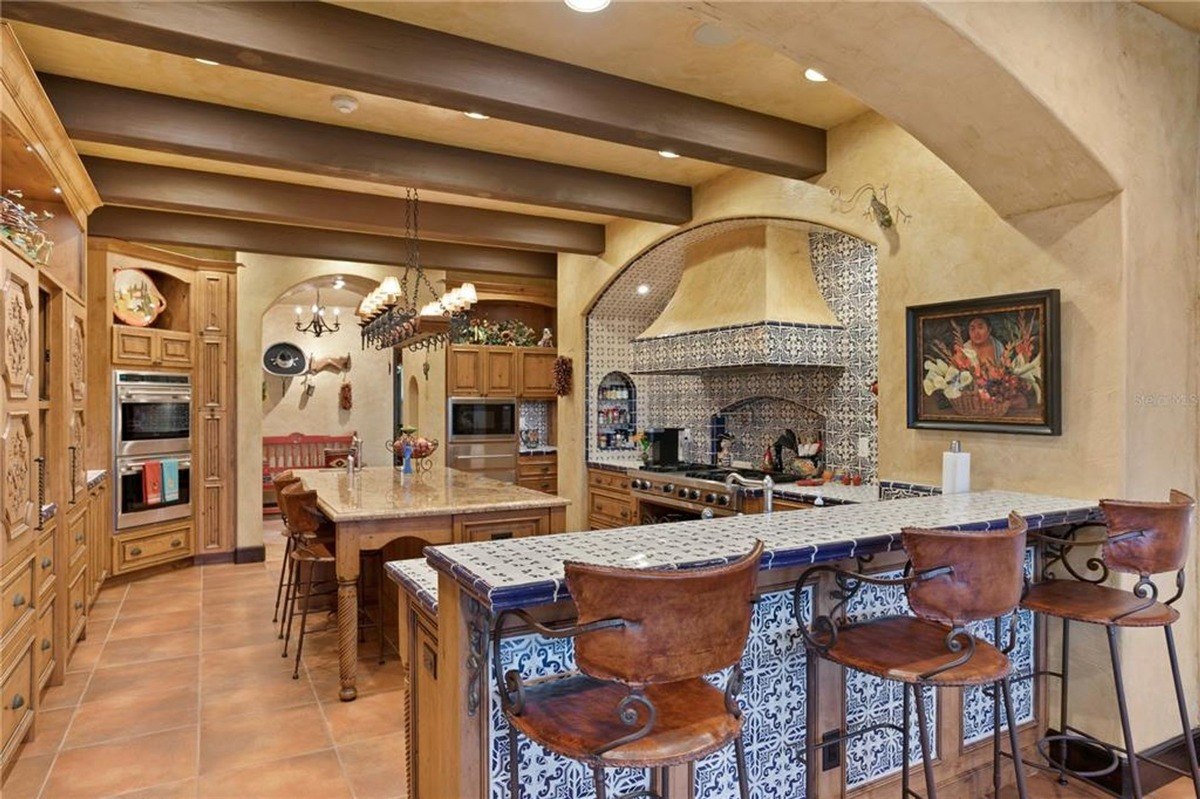 Kitchen features a large island with a granite countertop, a breakfast bar with tile backsplash, and exposed wooden beams.