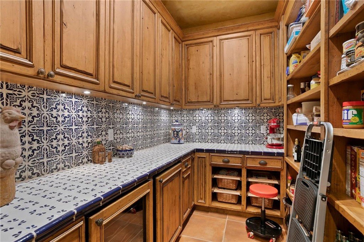 Pantry features wood cabinets, blue and white tile backsplash, and ample shelving for storage.