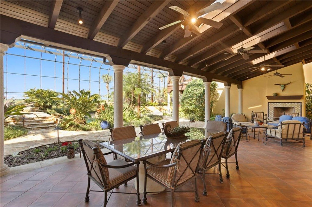 Covered patio features a dining area with a glass-top table, seating area with lounge chairs, and views of a lush backyard.