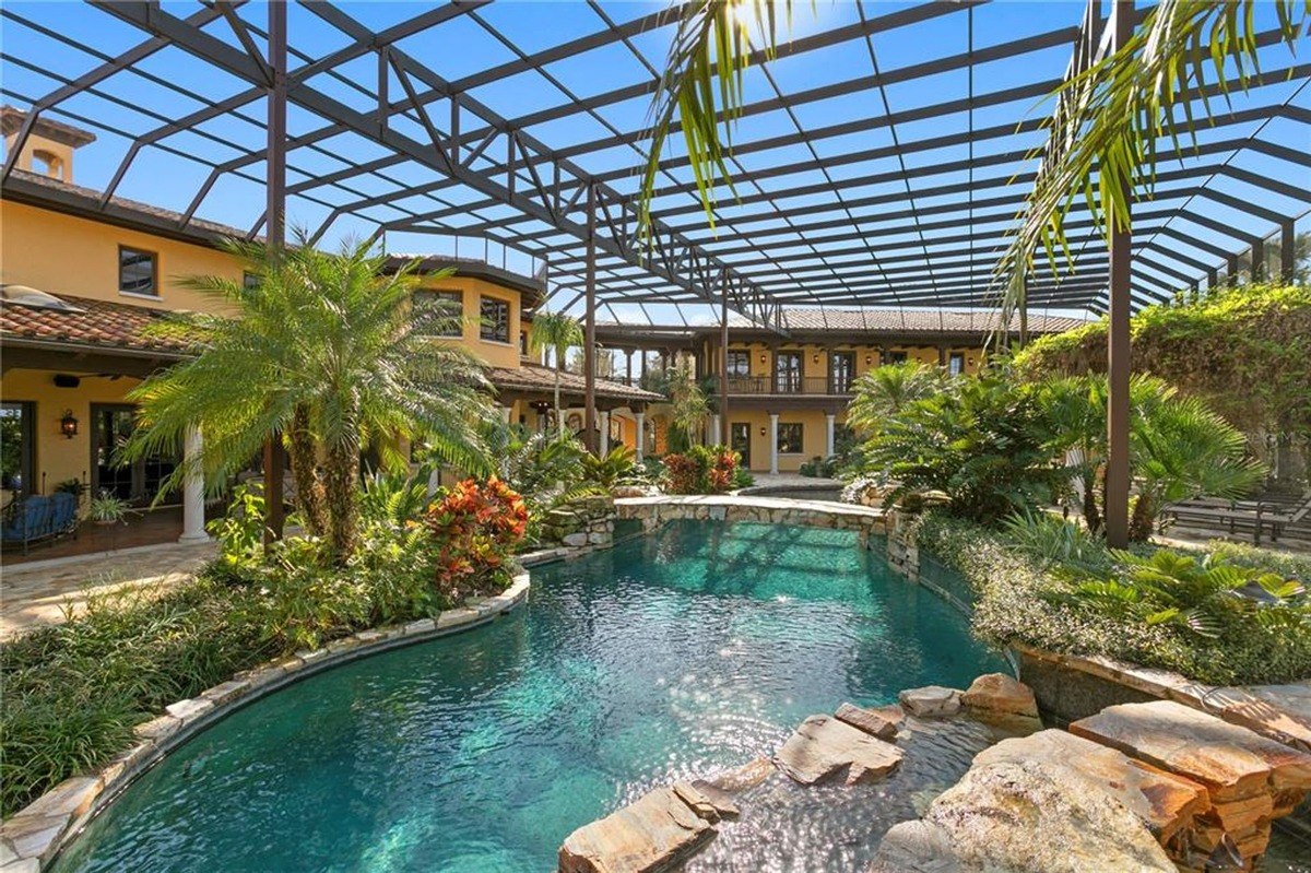 Resort-style pool with a rock waterfall feature is surrounded by lush landscaping and a covered patio area.