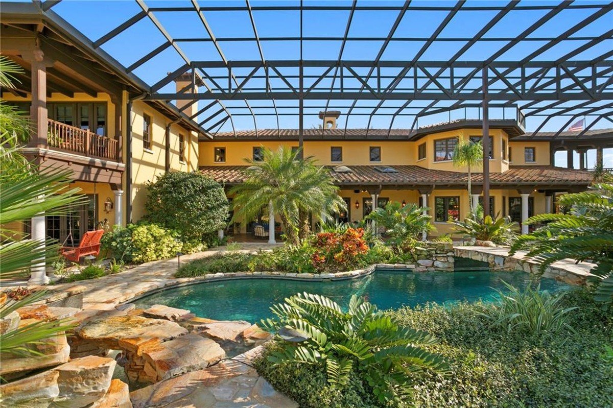 Resort-style pool with a rock waterfall feature is surrounded by lush landscaping and a covered patio area.