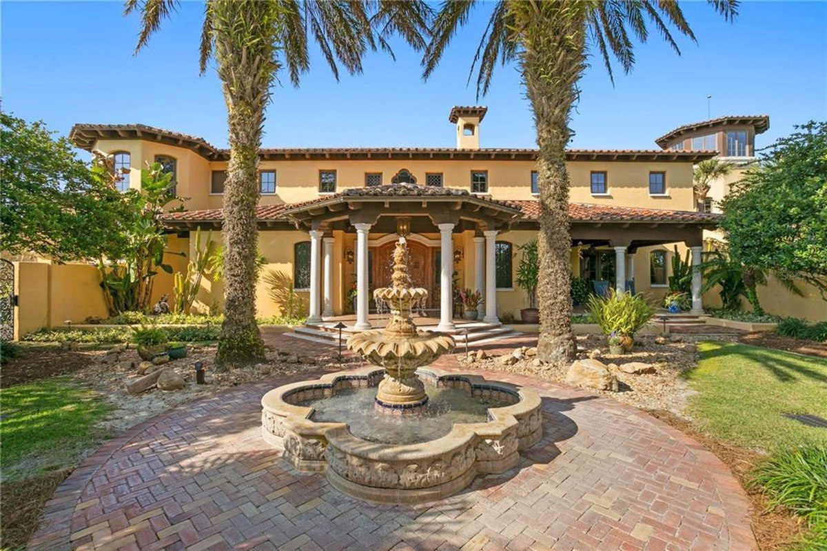 Mediterranean-style mansion features a grand entrance with a fountain and palm trees.