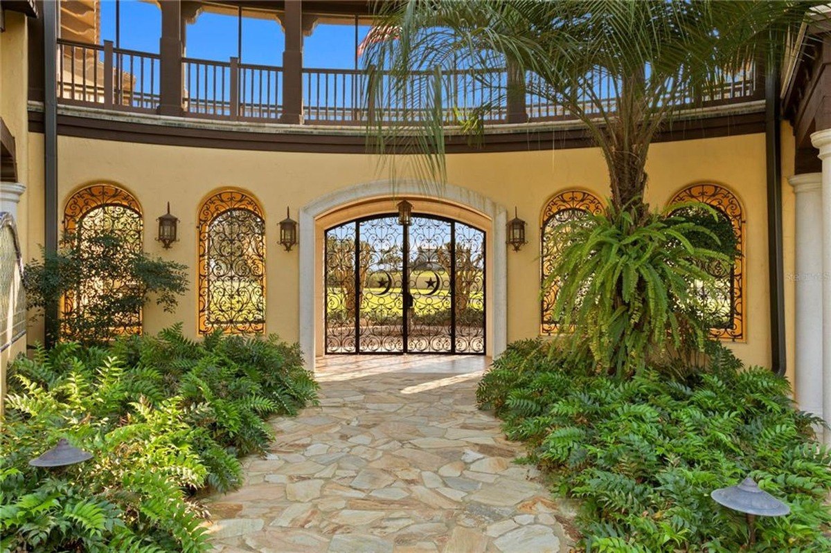 Koi pond with a small waterfall is situated in a courtyard next to a Mediterranean-style house with a second-story balcony.