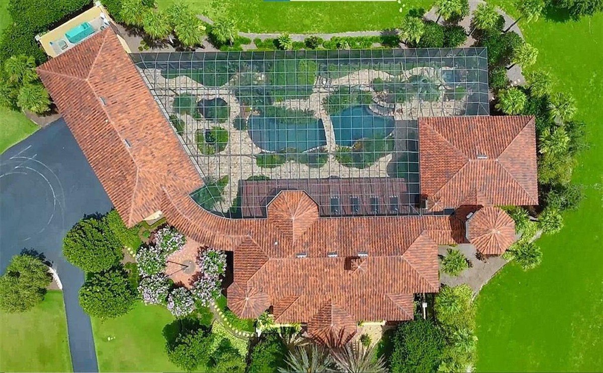 Aerial view shows a large house with a red tile roof, a pool area, and extensive landscaping.