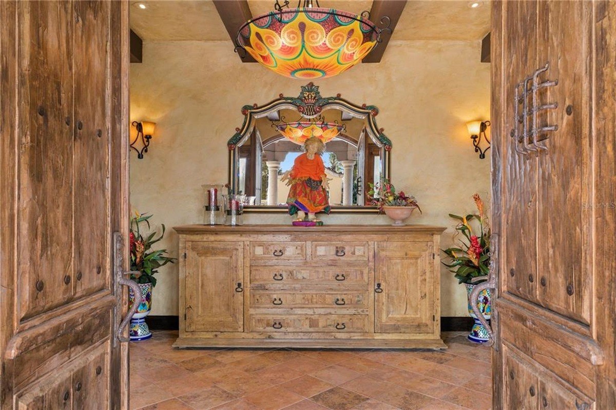 Entryway features rustic wooden doors, a large wooden cabinet, and a colorful chandelier.