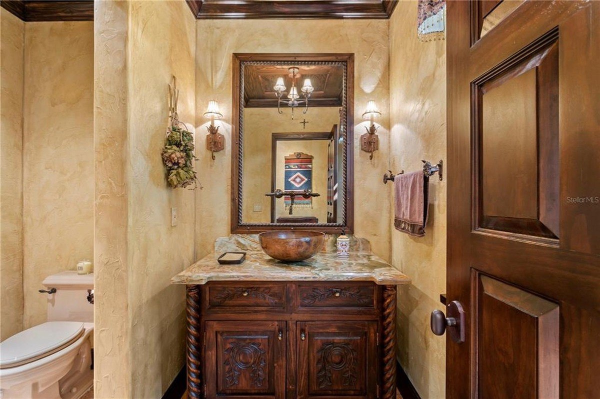 Powder room features a rustic vanity with intricate carvings, a copper sink, and textured walls.