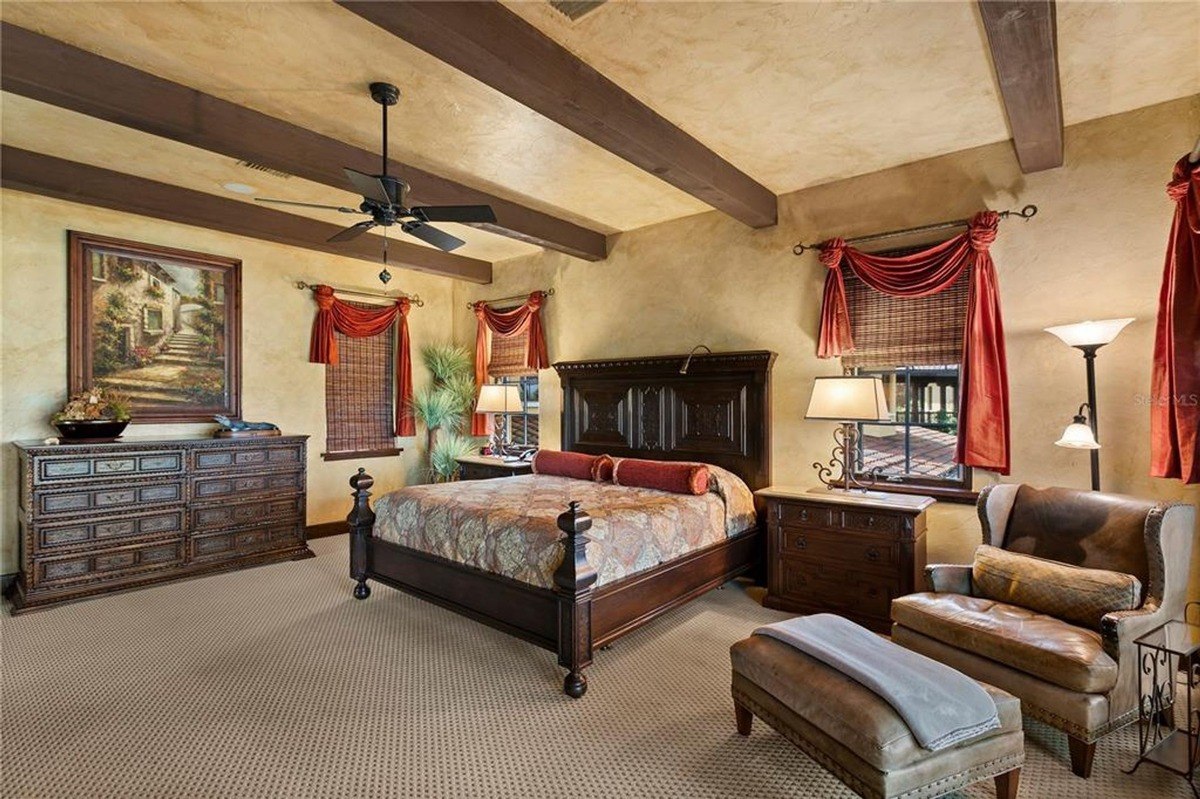 Master bedroom features a large four-poster bed, a leather armchair, and exposed wooden beams.