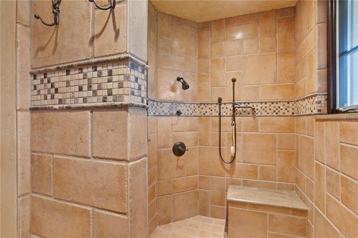 Shower features large, light-colored tiles, a built-in seat, and decorative mosaic borders.