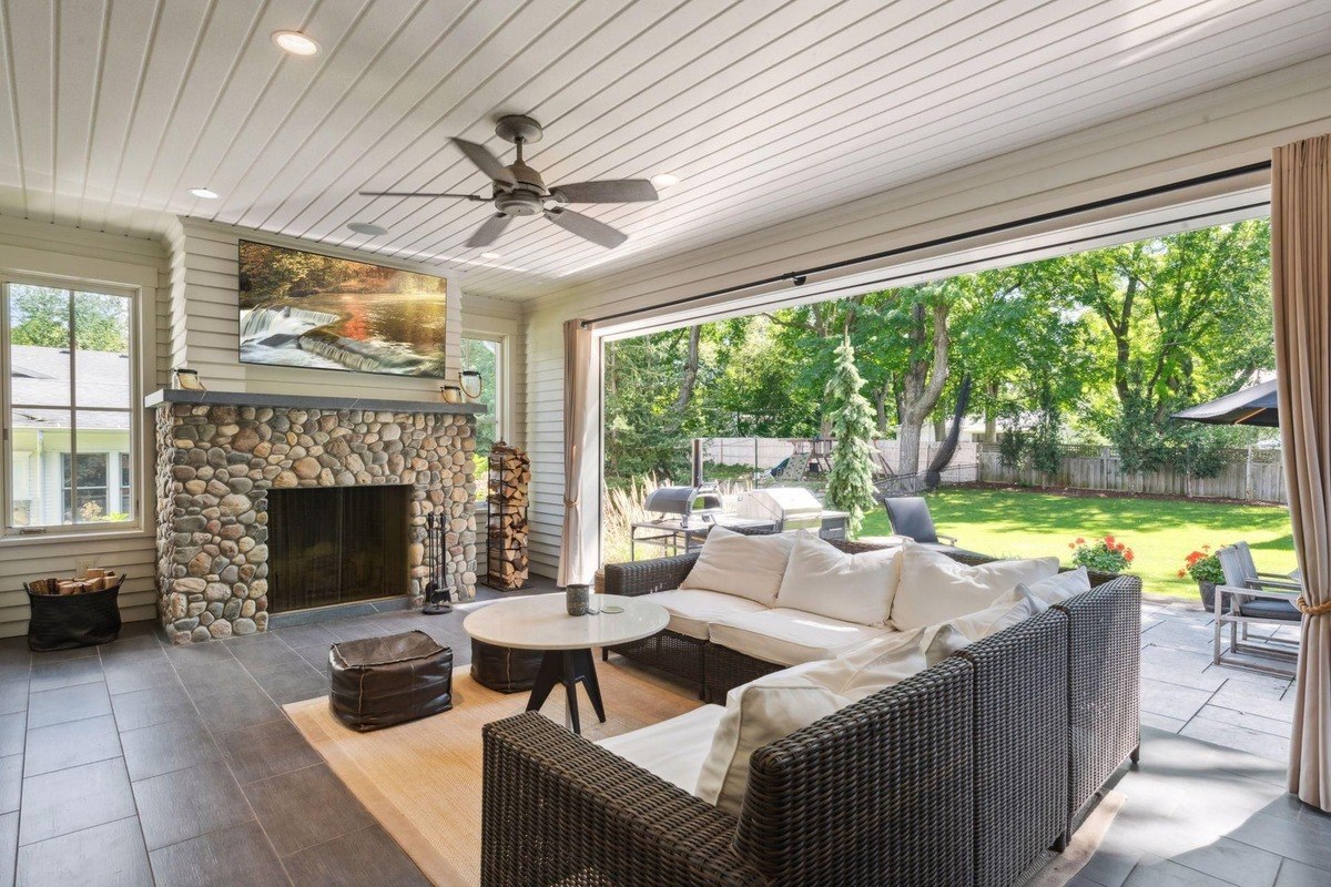 Screened patio a stone fireplace, cushioned seating, and an open view of the backyard.