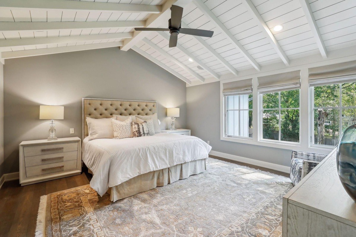 Spacious bedroom with vaulted ceilings, a tufted headboard, and large windows bringing in natural light