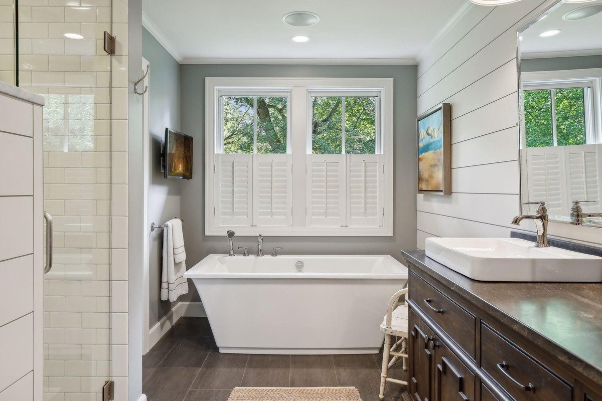 Primary bathroom with a freestanding bathtub, shiplap walls, and plantation shutters over the windows.