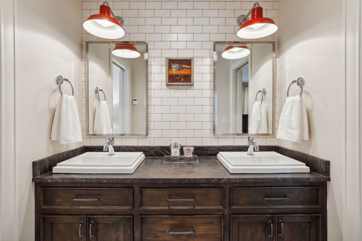 Shared bathroom a double vanity bathroom with white subway tile walls, dark wood cabinetry, and red industrial-style pendant lights.