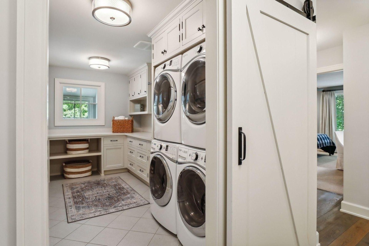 Laundry room with a double set of stacked washers and dryers, ample cabinetry, and a folding area.