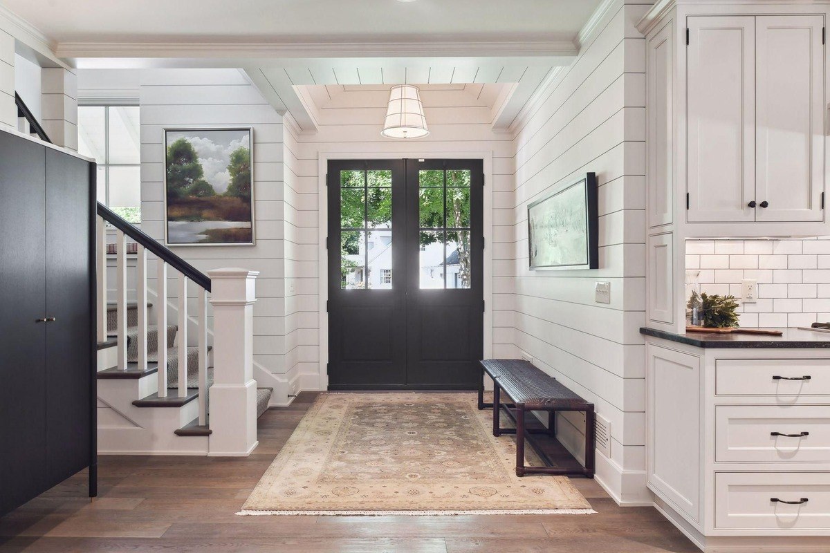 .Entryway a bright foyer with white shiplap walls, a decorative rug, and a staircase.