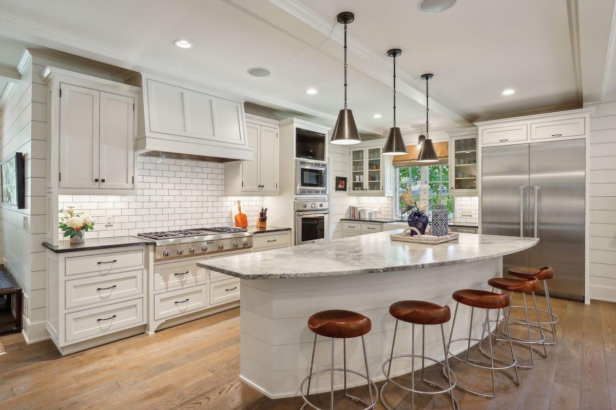 Bright kitchen with a large marble island, white cabinets, and pendant lighting.