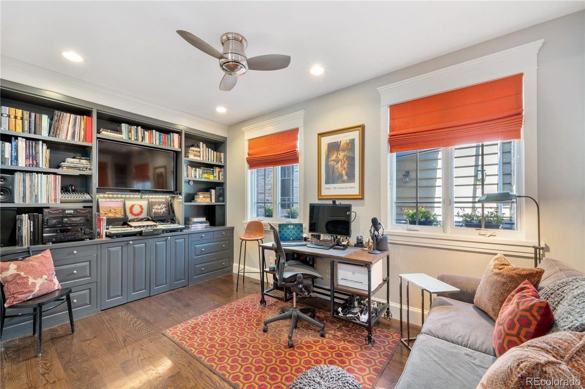 Room has built-in bookshelves, TV, desk, and seating area with ceiling fan.