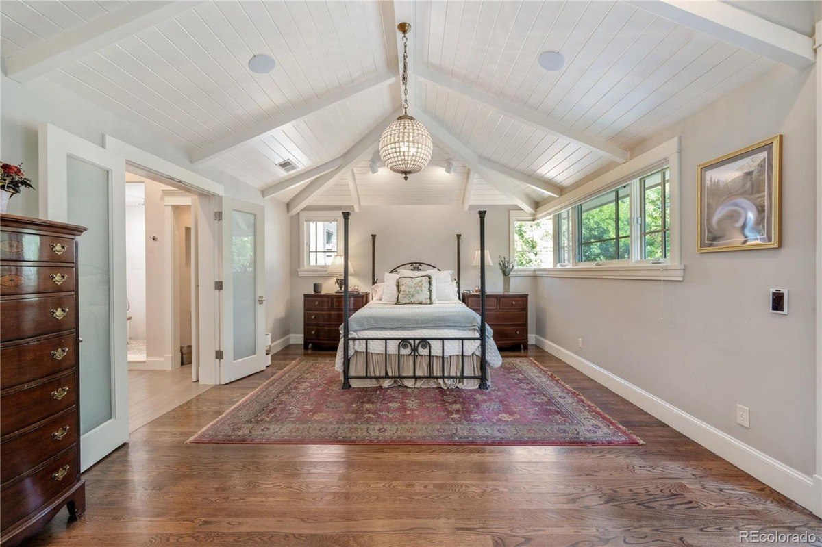 Bedroom with wood floors, vaulted ceiling with chandelier, and bed with metal frame.