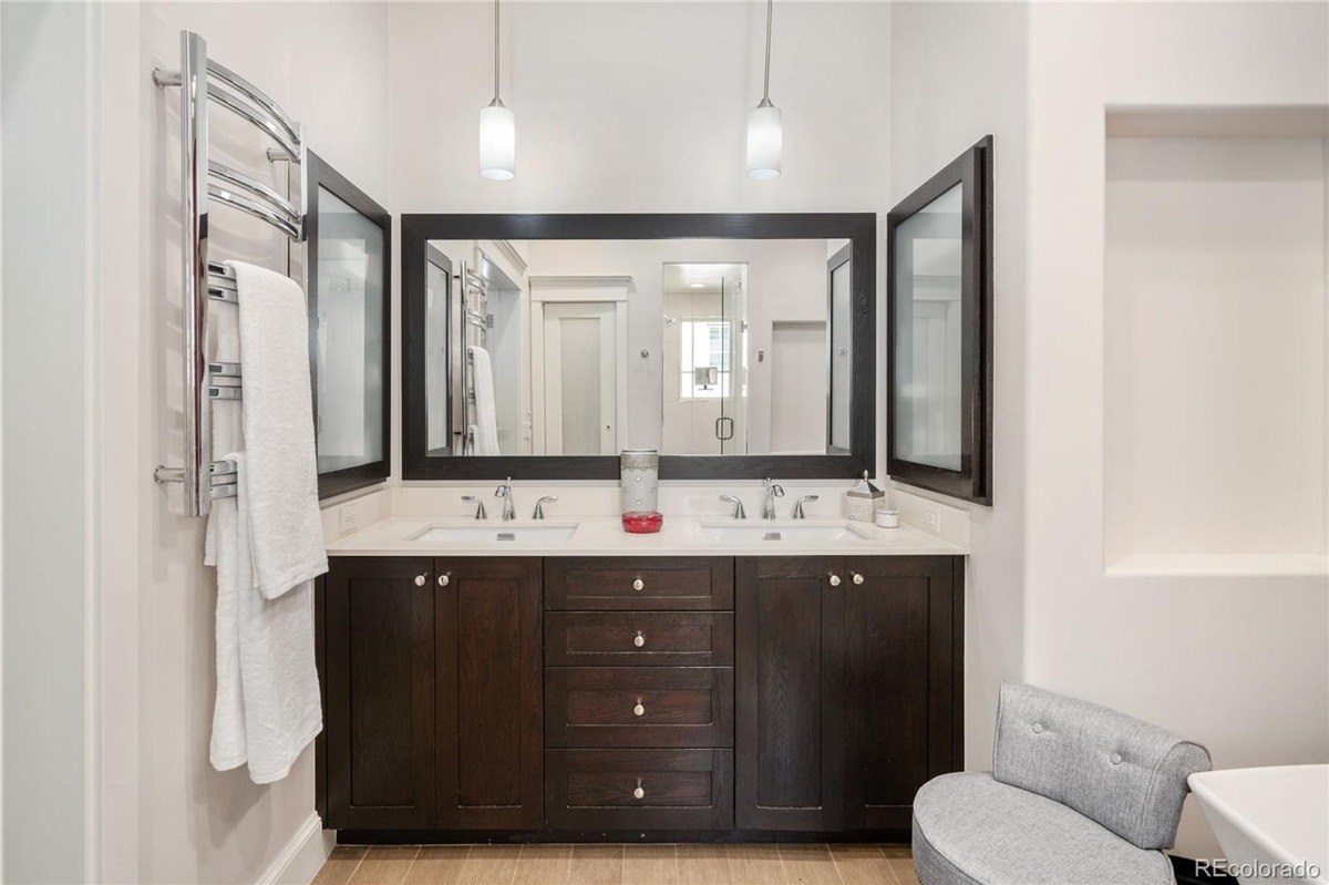 Bathroom with double vanity with dark cabinets, large mirror, and heated towel rack.