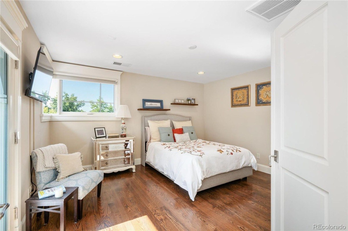 Bedroom with hardwood floors, bed with white bedding, and sitting area with TV.