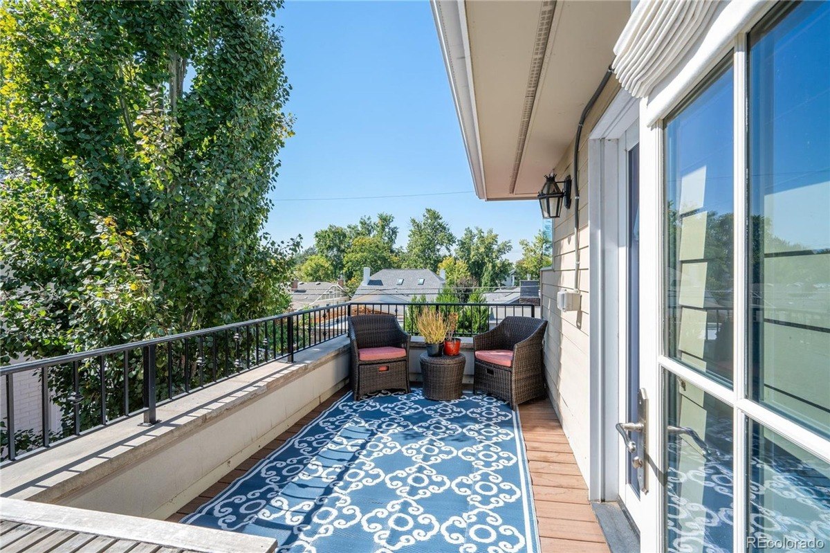 Balcony has two wicker chairs, small table, and patterned rug.