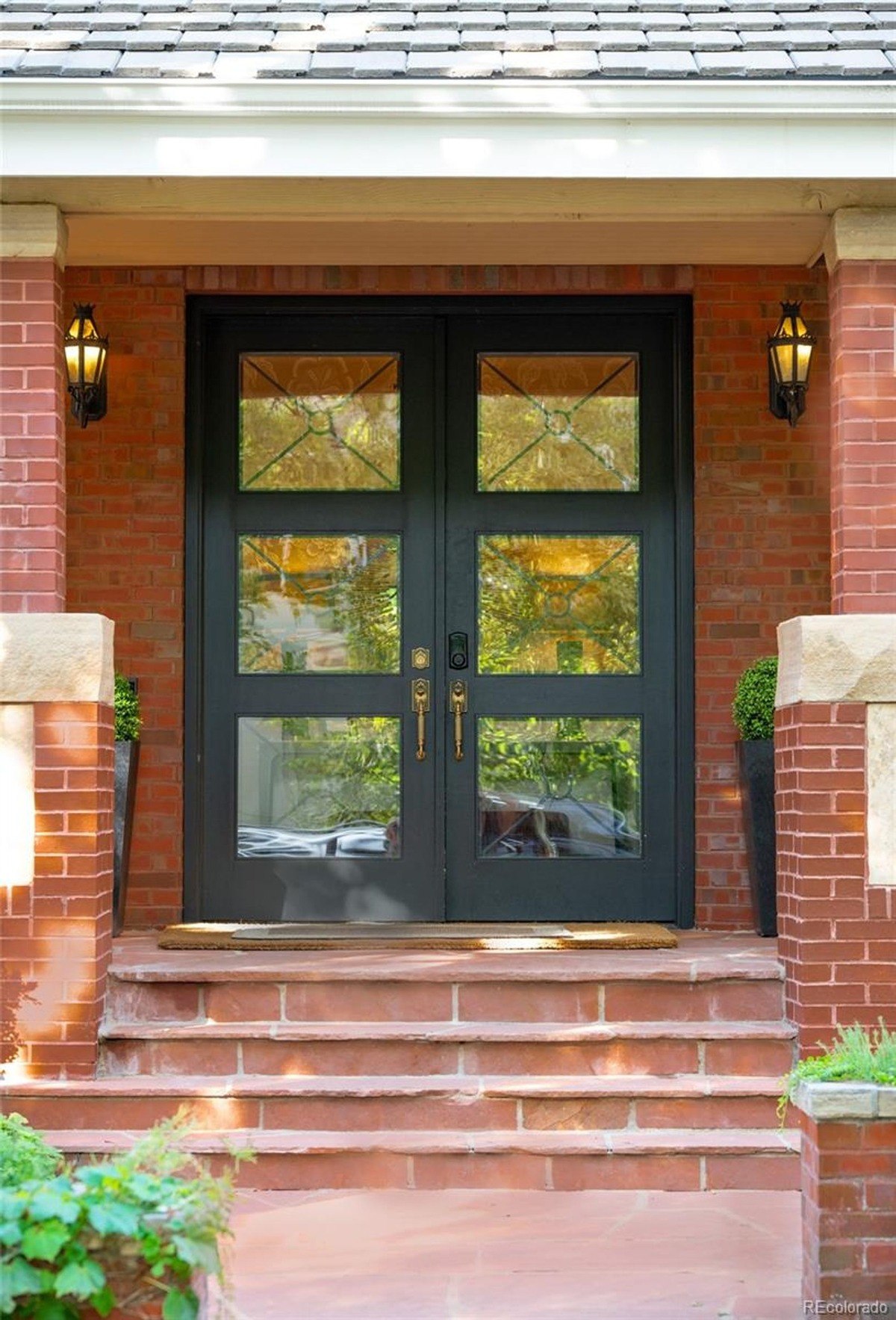 Dark double doors, accented with glass panes, create a dramatic entryway, highlighted by flanking lights and planters.