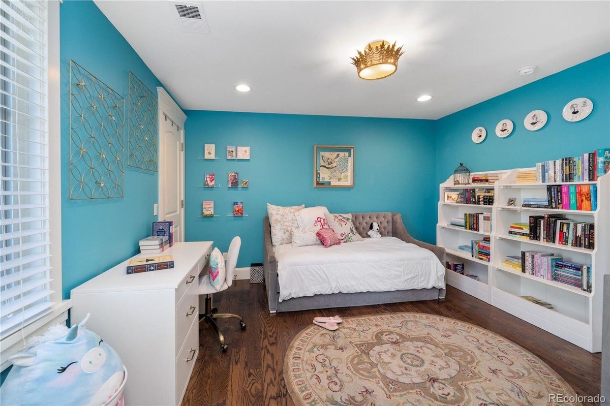 Child's bedroom with teal walls, daybed, desk, bookshelves, and area rug.