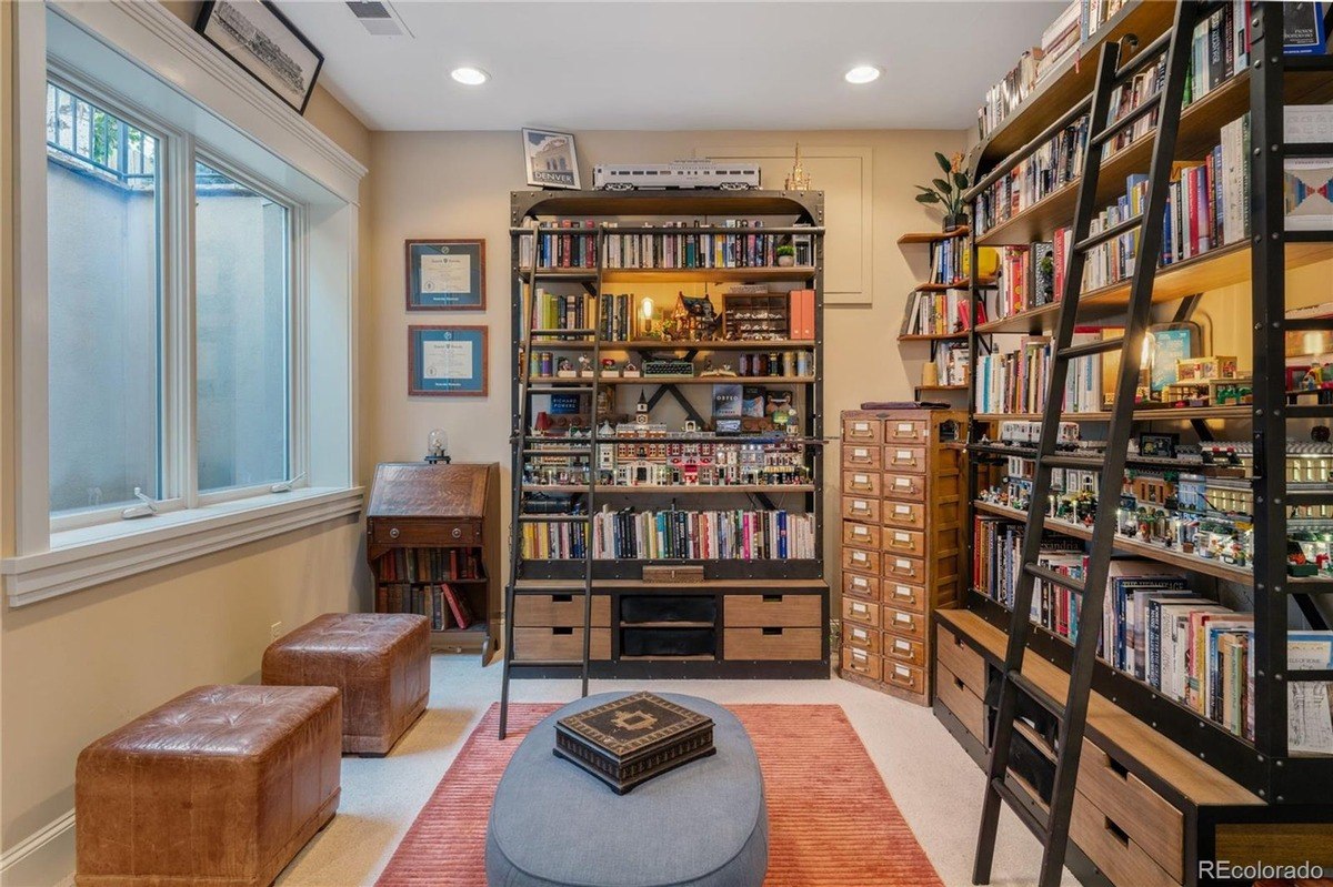 Room with large bookshelves, window seat with ottomans, and area rug.