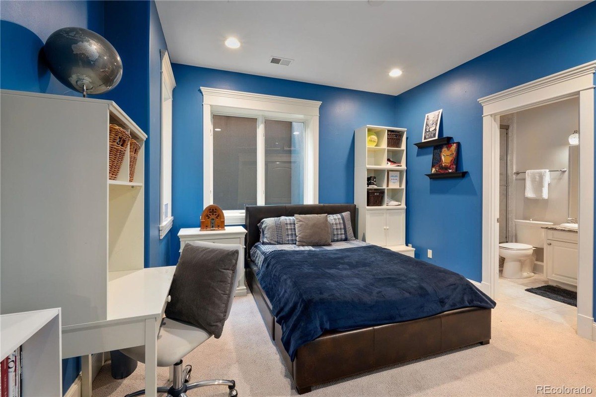 Bedroom has blue walls, bed with navy bedding, desk, and globe.