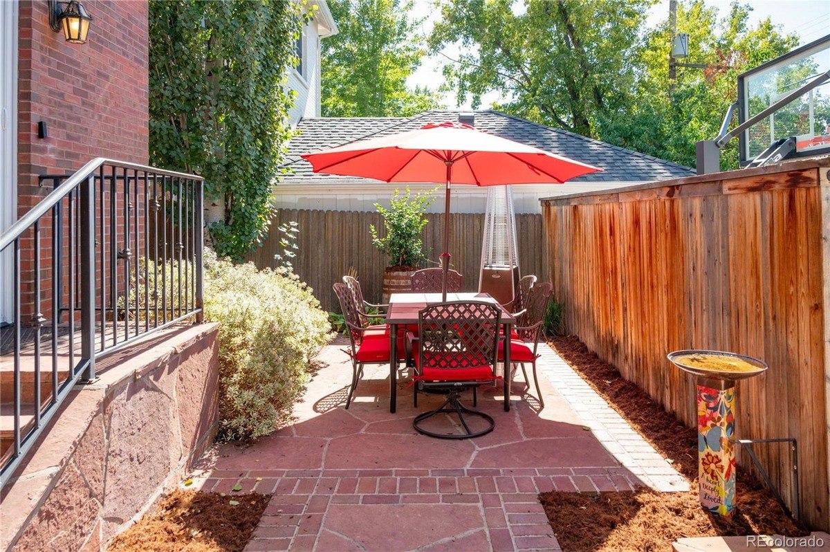 Patio with red brick pavers, metal table and chairs under umbrella, and wood fence.