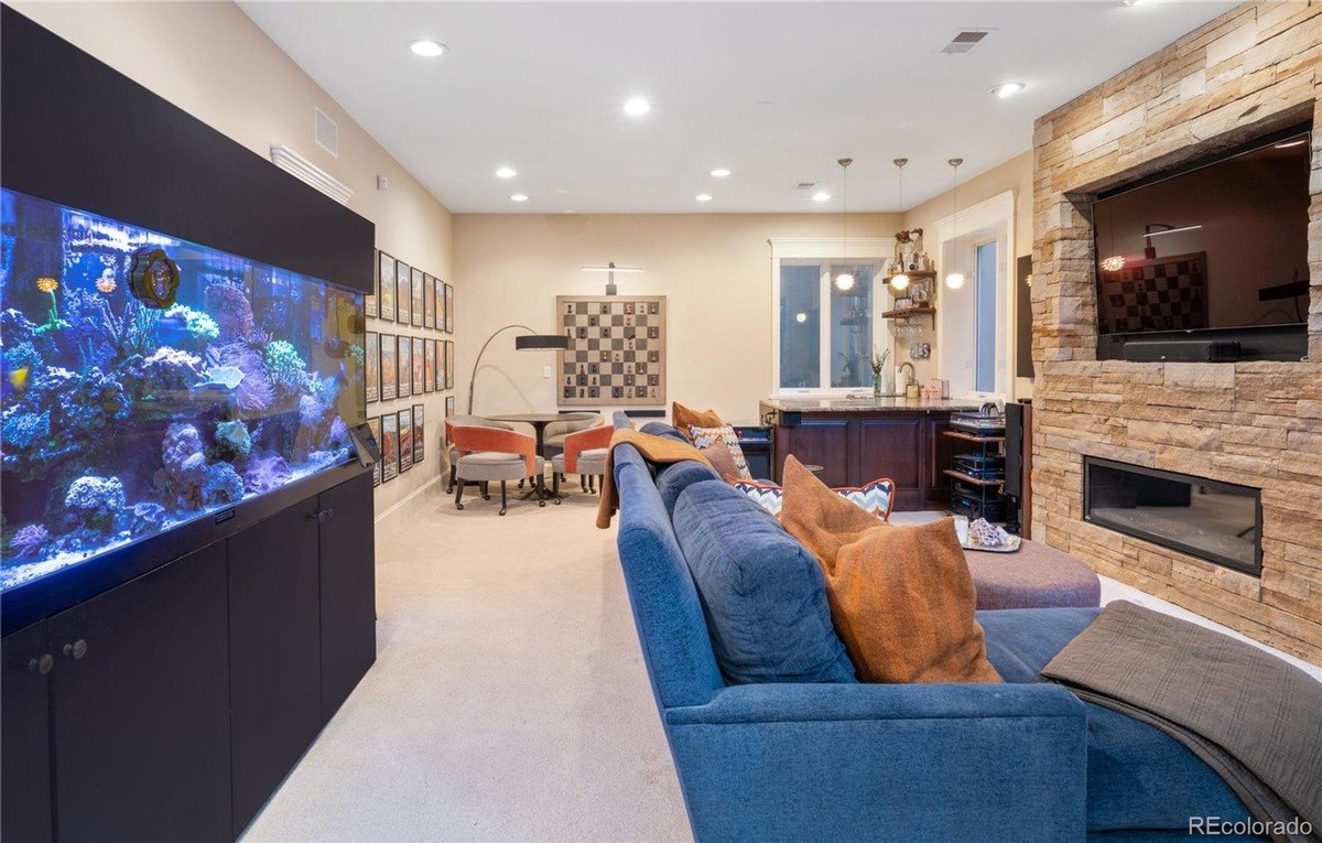 Game room has large aquarium, sectional sofa, stone fireplace with TV, and game table.