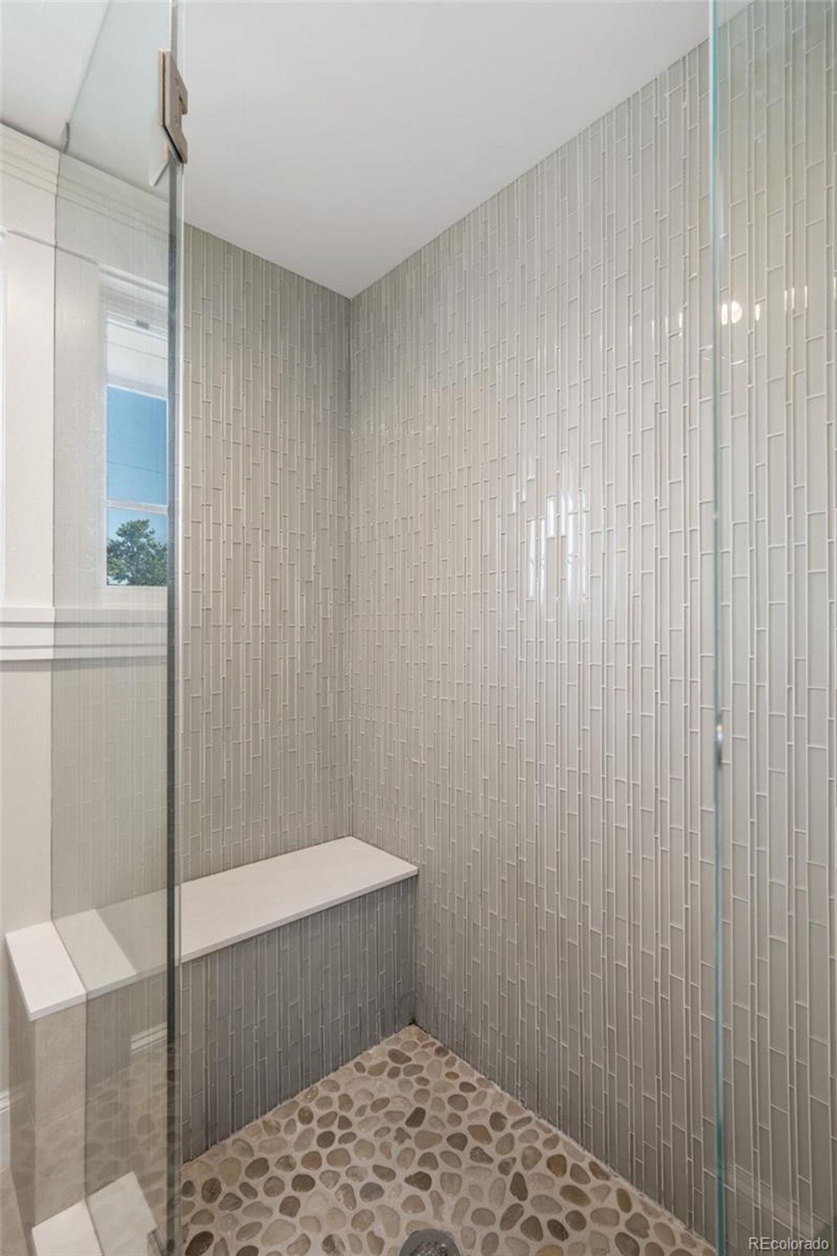 Shower with glass enclosure, built-in seat, and pebble floor.