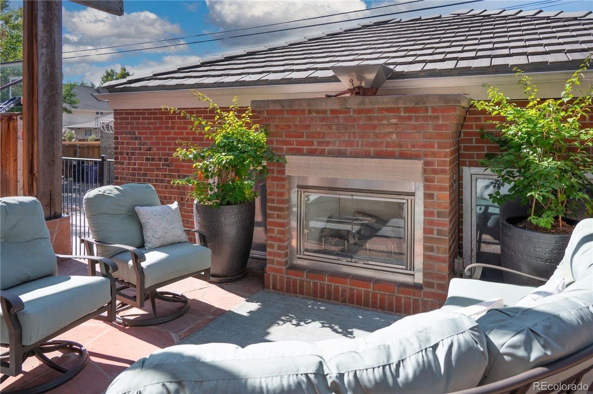 Outdoor patio has brick fireplace, seating area with cushions, and potted plants.