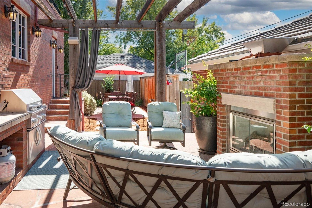 Outdoor patio with curved seating area, brick fireplace, pergola, and grill.