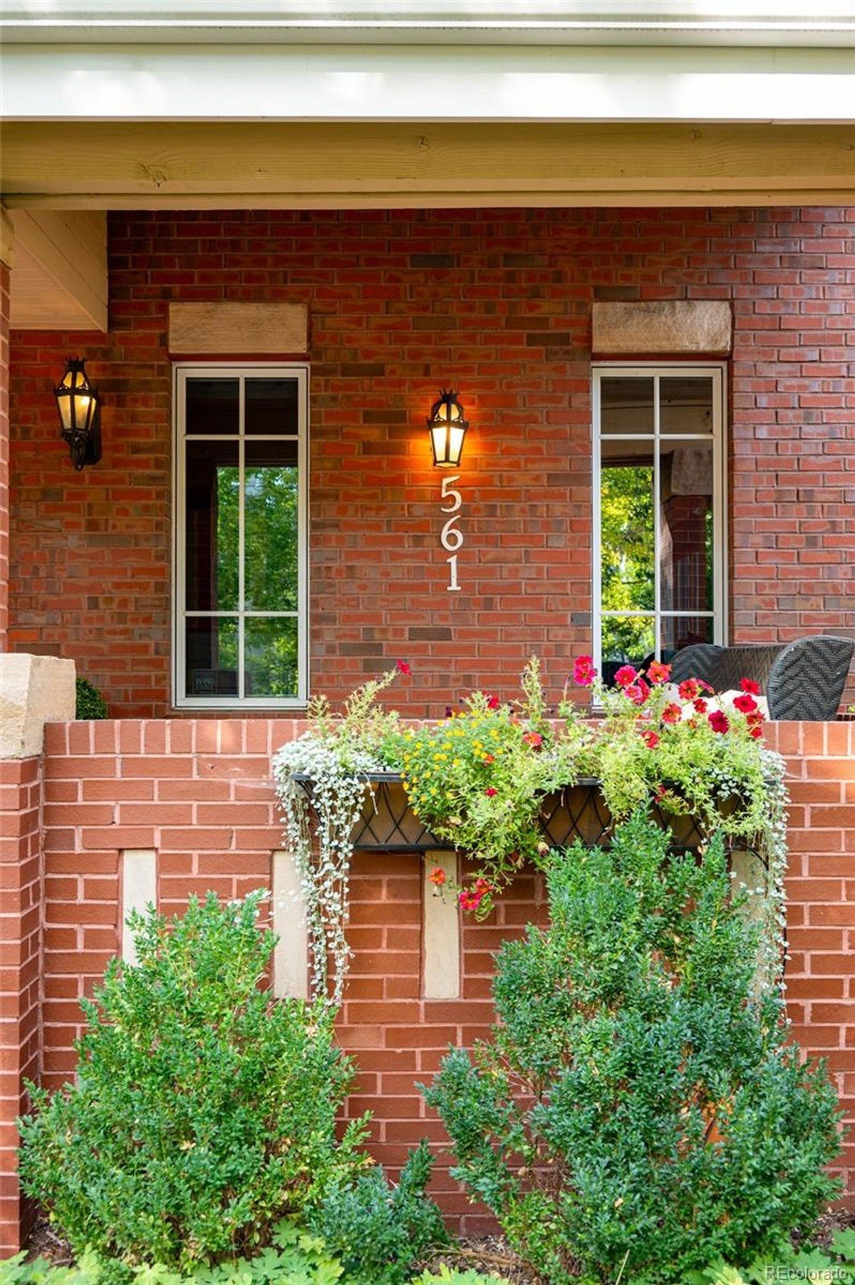 Brick building has porch with flower boxes, light fixtures, and windows.