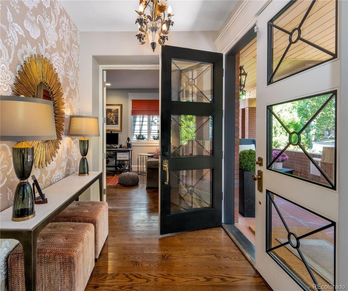 Entryway has patterned wallpaper, console table, and dark door with glass panes.