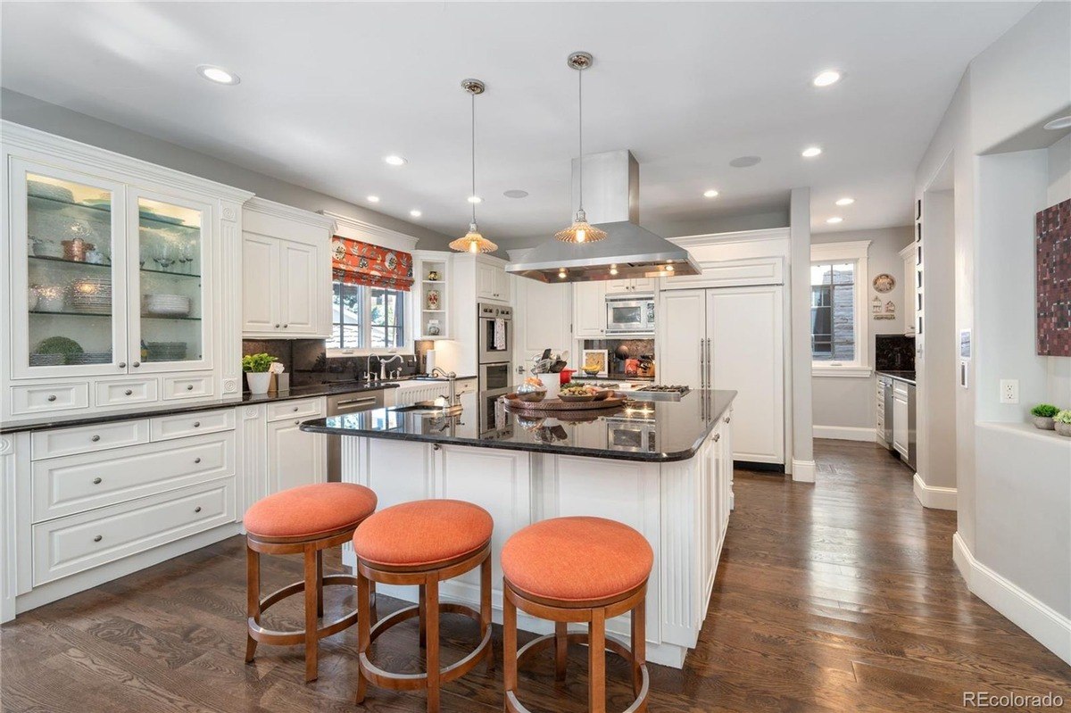 Kitchen has white cabinets, granite island with stools, and hardwood floors.