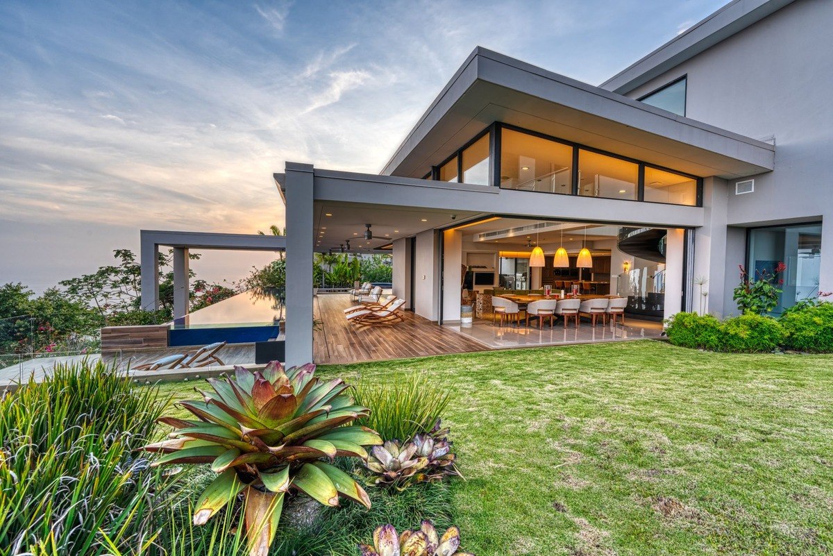 Modern home has infinity pool, large windows, and landscaped yard.