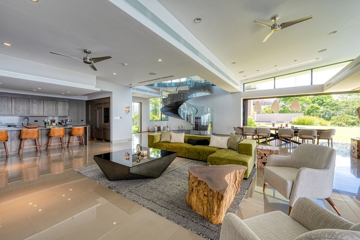 Open-concept living area has green sectional sofa, kitchen, and spiral staircase.