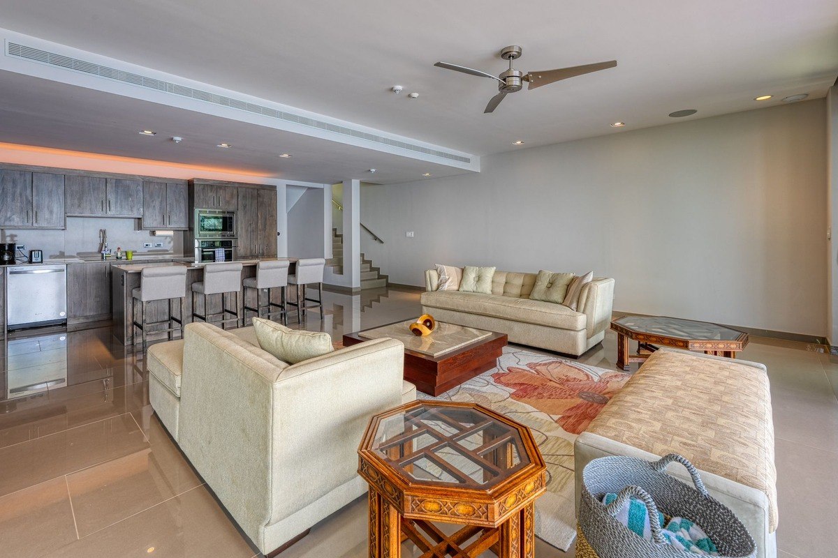 Living room has beige sofas, kitchen, and ceiling fan.