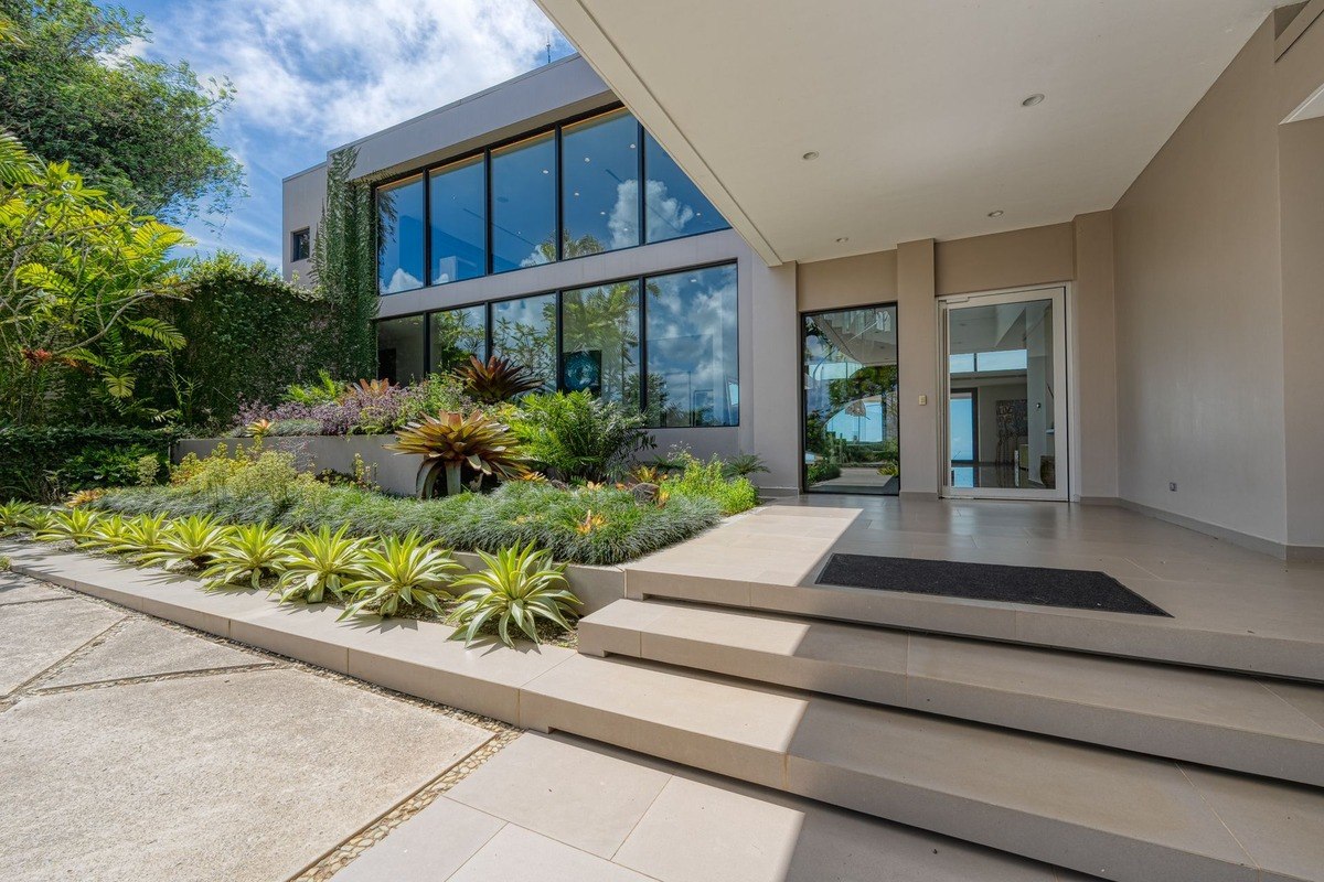 Modern home entrance has large windows, landscaped walkway, and stairs.