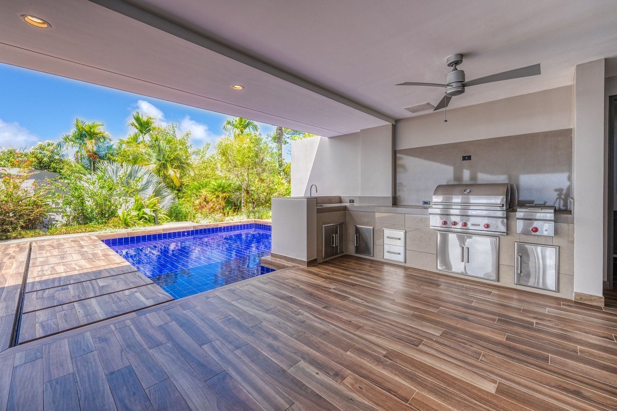 Outdoor kitchen has stainless steel appliances and pool view.