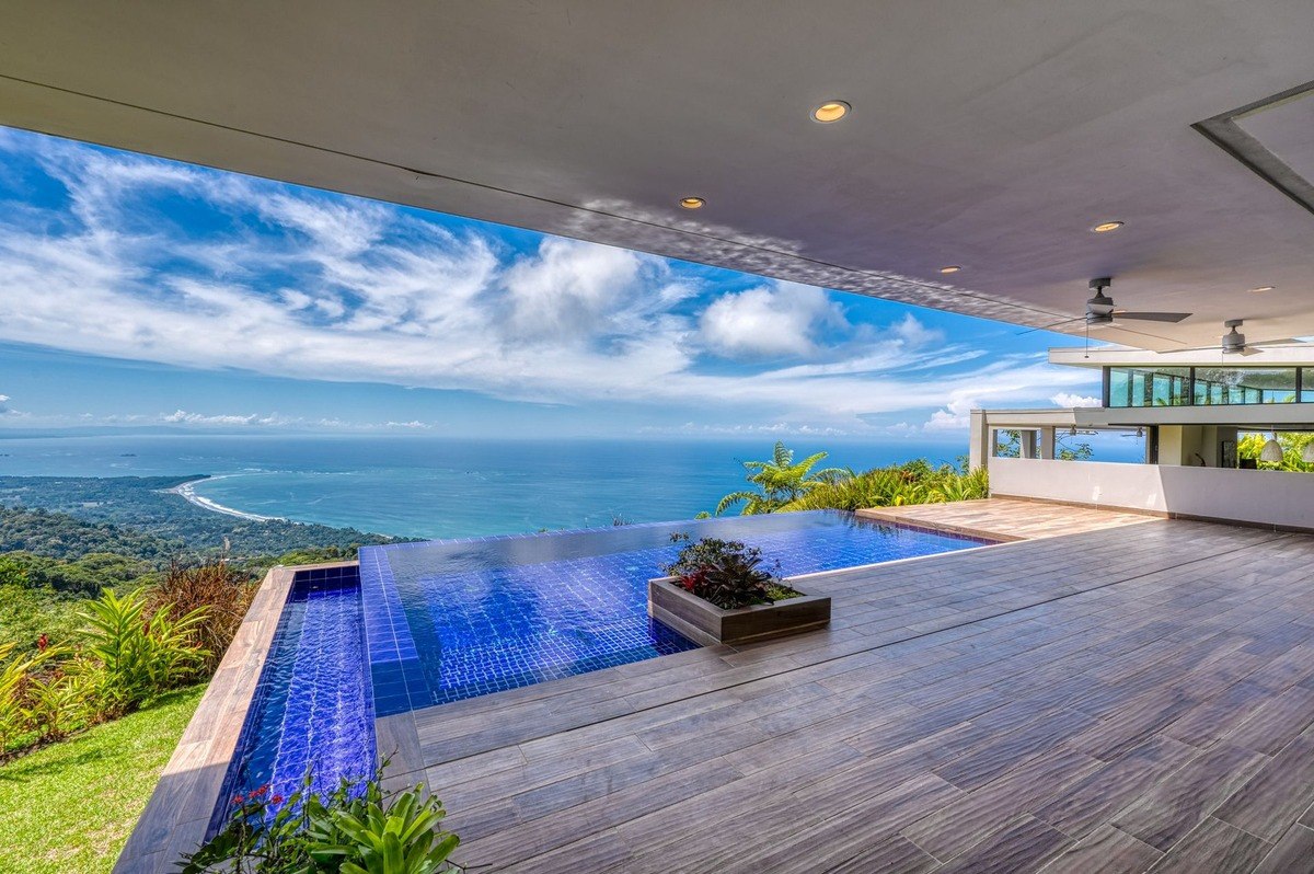 Infinity pool has ocean view and tropical landscaping.