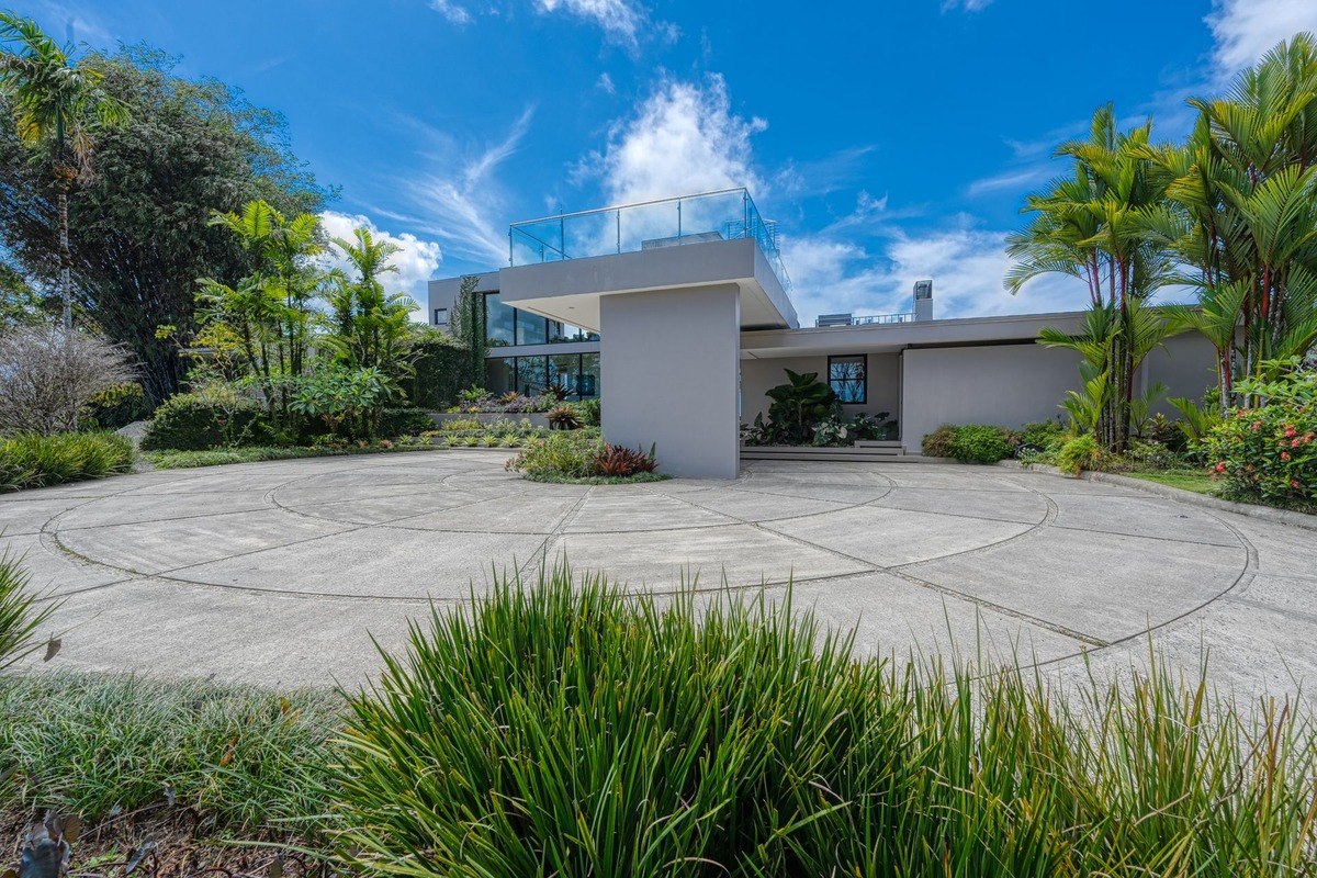 Modern home has circular driveway and tropical landscaping.