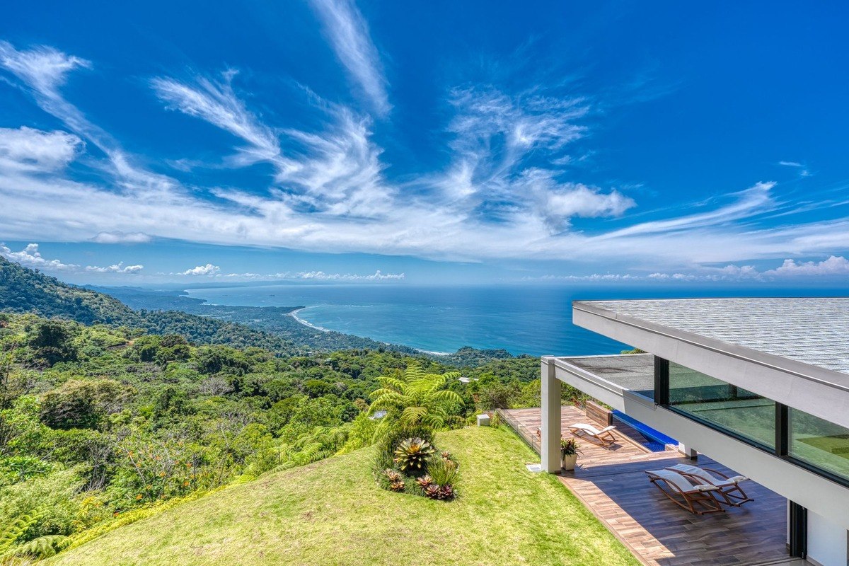 Ocean view home has large windows and tropical landscaping.