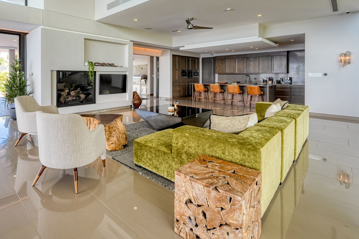 Living room has large green sectional sofa, fireplace, and kitchen view.