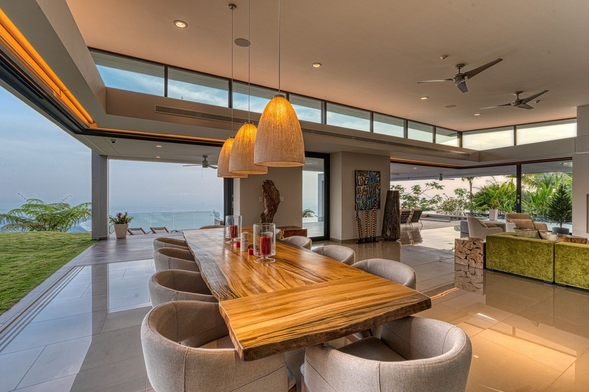 Dining room has large wood table, ocean view, and modern lighting.