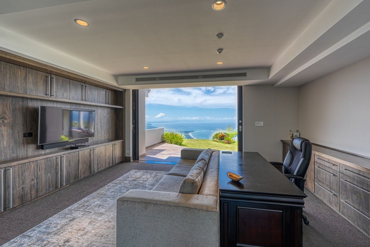 Home office has large built-in shelving, ocean view, and comfortable seating.