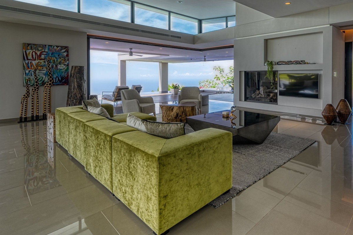 Living room has large green sectional sofa, ocean view, and fireplace.